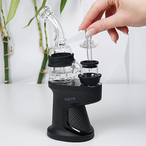 Ispire Daab Kit sobre una mesa mientras una mujer sostiene un carb cap de vidrio cerca de la cámara de calentamiento