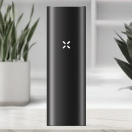 Vista frontal del vaporizador New PAX Mini en color Onyx, con el logotipo PAX iluminado sobre un cuerpo de aluminio negro elegante, colocado en un entorno interior moderno.