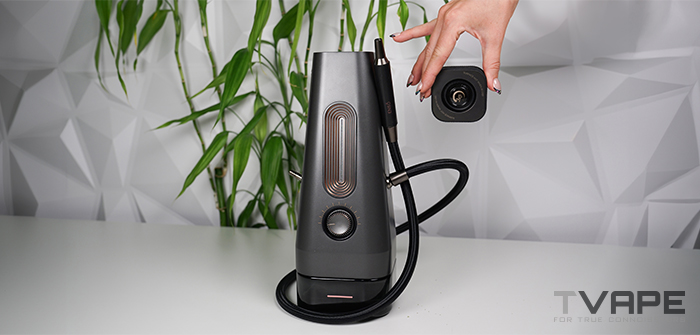 Se ve cómo se retira a mano la tapa térmica de cristal extraíble (Glass ThermoCap) de la shisha eléctrica AirVape Enso 2026, dejando a la vista la cámara de calentamiento abierta y la manguera de vapor conectada