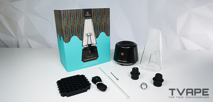 La Tronian Omegatron 2 desembalada junto a su caja: base negra, vaso de vidrio, cubitera de silicona con forma de panal, cable USB-C, pajita de vidrio, herramienta de carga, tapa de la cámara para cera, tapa 510 y cámara de calentamiento BurstHit All Wall.